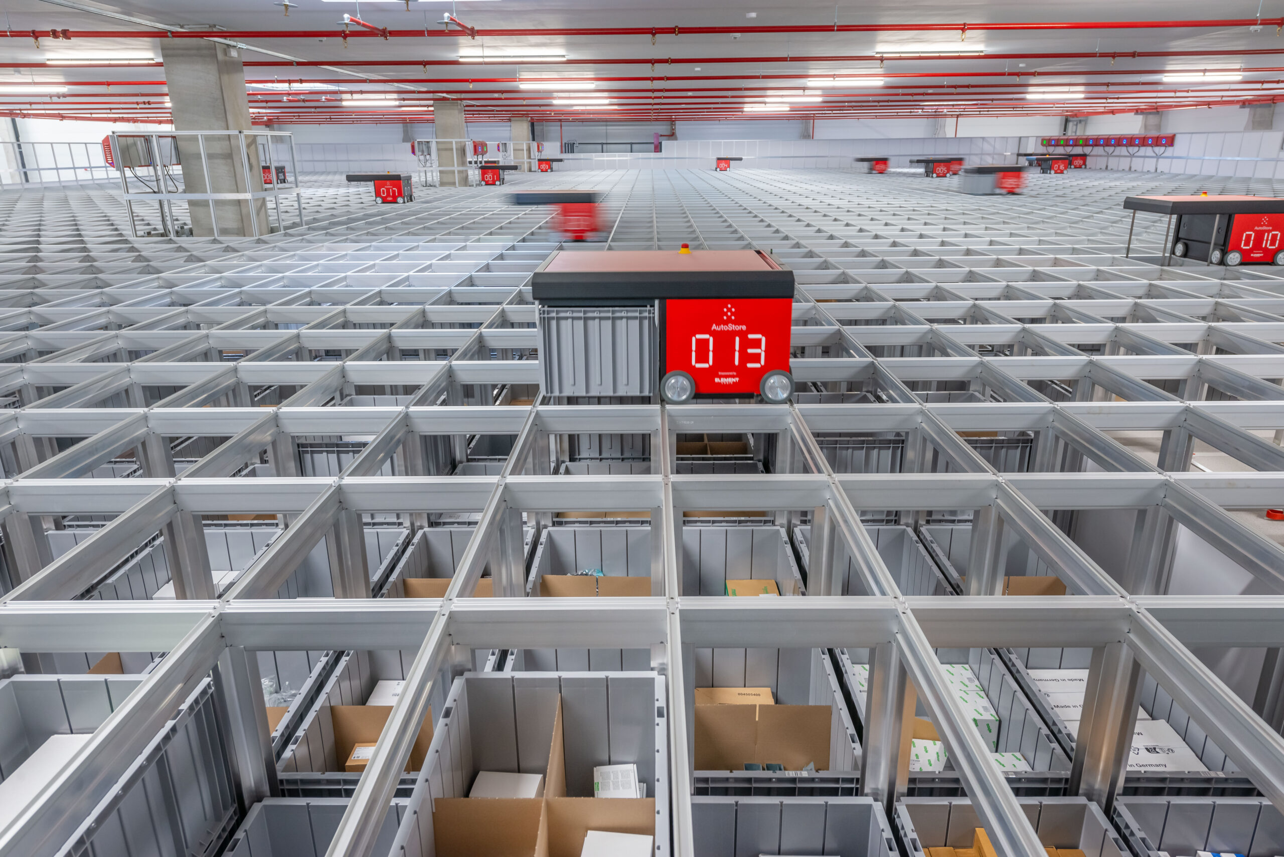 Robots AutoStore operando sobre la rejilla del sistema en un almacén automatizado, con cubetas de almacenamiento bajo la estructura.