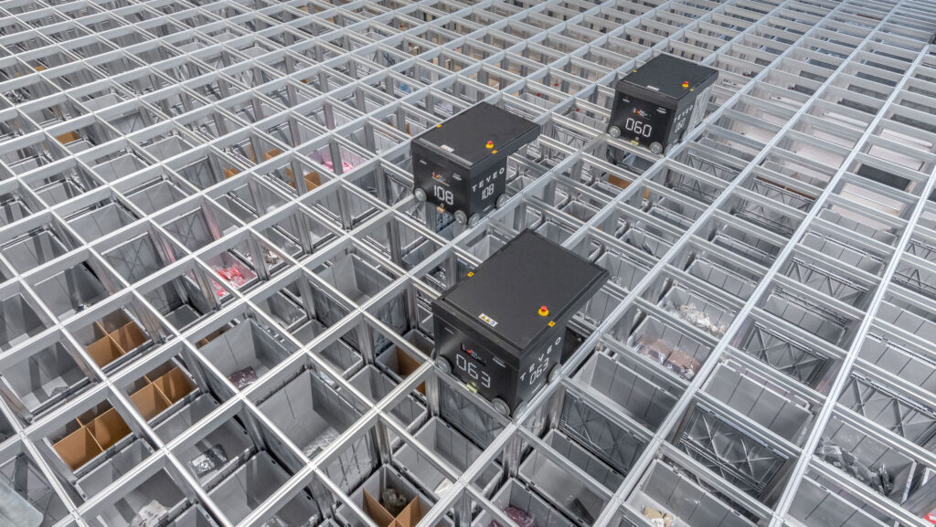 Robots AutoStore operan sobre una cuadrícula de almacenamiento con cubetas visibles en un sistema automatizado de alta densidad.