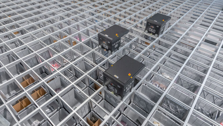 Robots AutoStore operan sobre una cuadrícula de almacenamiento con cubetas visibles en un sistema automatizado de alta densidad.