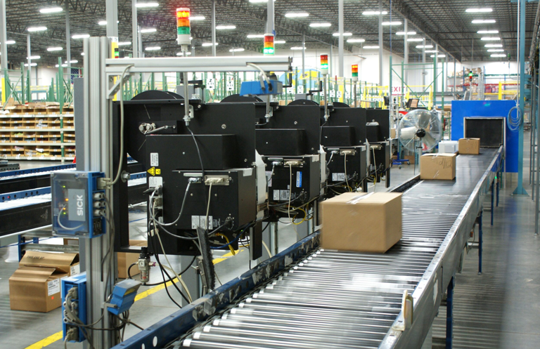 Cajas avanzan por una línea de rodillos con equipos de clasificación automatizada en un almacén industrial.