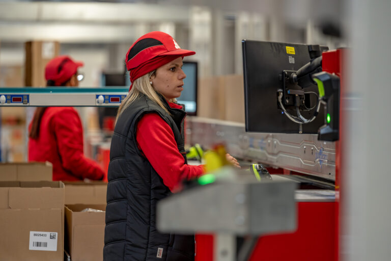 Operaria trabaja frente a una pantalla en una estación de picking mientras gestiona pedidos en un almacén automatizado.