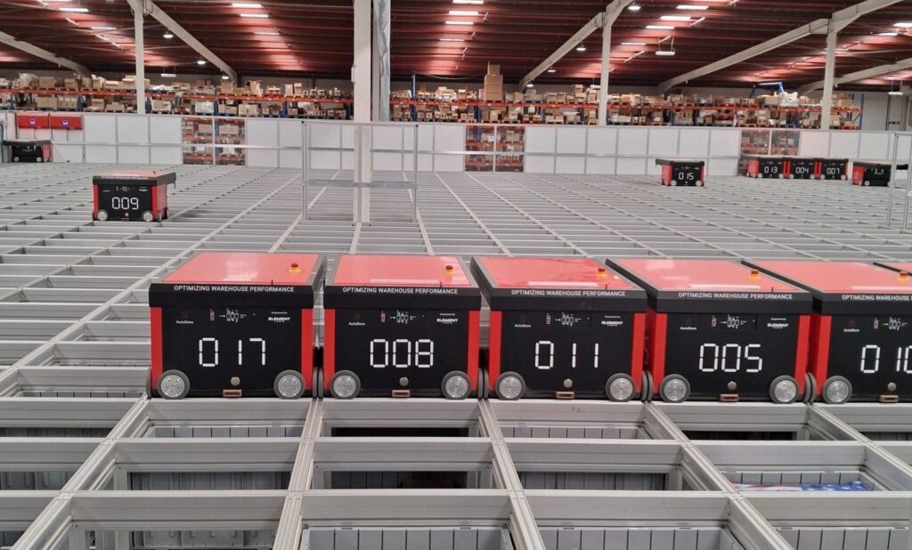 Robots AutoStore desplazándose sobre la rejilla del sistema de almacenaje en un almacén, durante operaciones de picking.