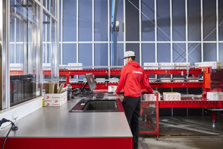 Operario trabajando en una estación de preparación de pedidos con transportadores en una instalación automatizada de farmacia.