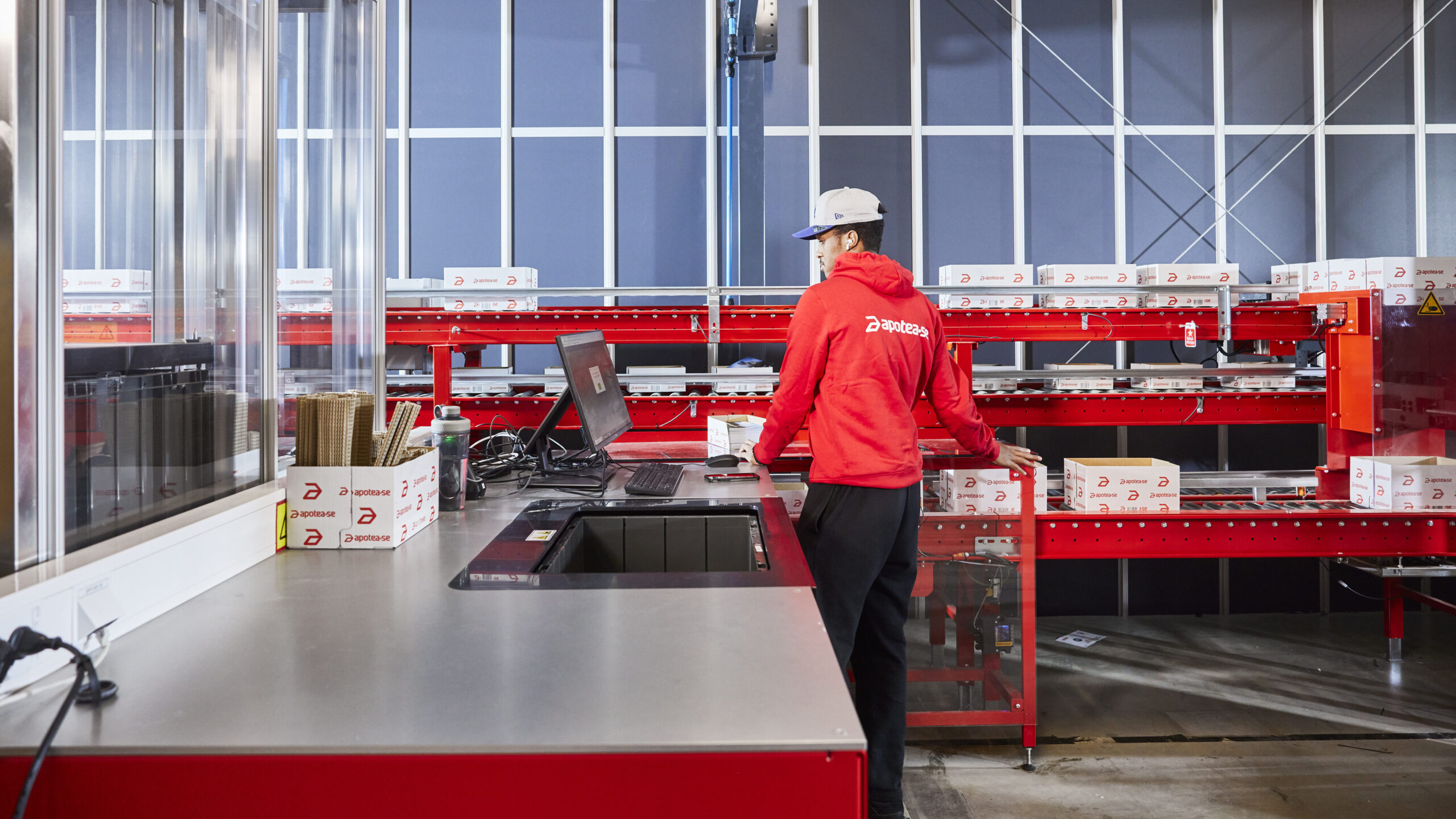 Operario trabajando en una estación de preparación de pedidos con transportadores en una instalación automatizada de farmacia.