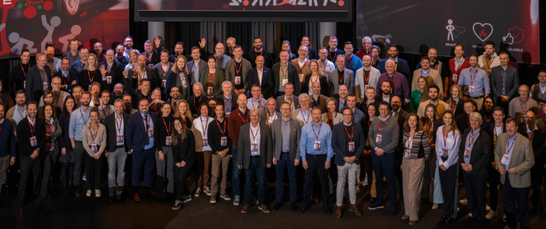 Foto de grupo de asistentes en un evento corporativo, posando en un auditorio con acreditaciones.