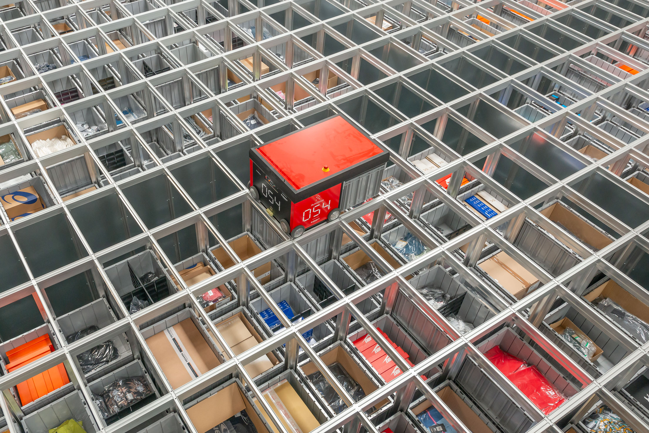 Sistema AutoStore con robot desplazándose sobre la cuadrícula de almacenamiento y cubetas con productos en un almacén automatizado.