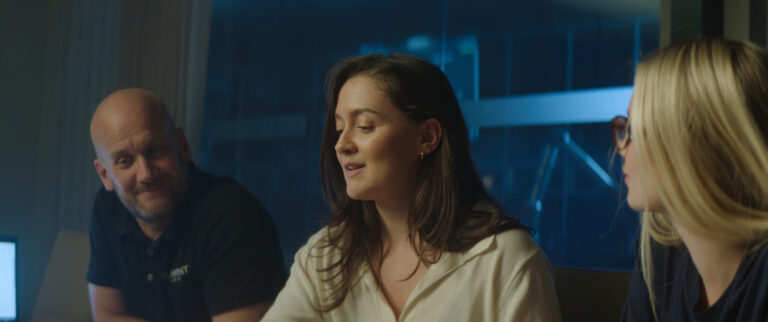 Tres personas en una reunión en una sala, conversando alrededor de una mesa en un entorno profesional.