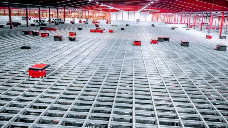 Robots rojos AutoStore desplazándose por encima de una rejilla de aluminio