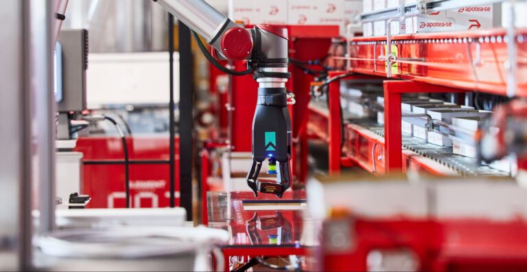 Brazo robótico de Element Logic operando en una estación automatizada con cajas en estantería.