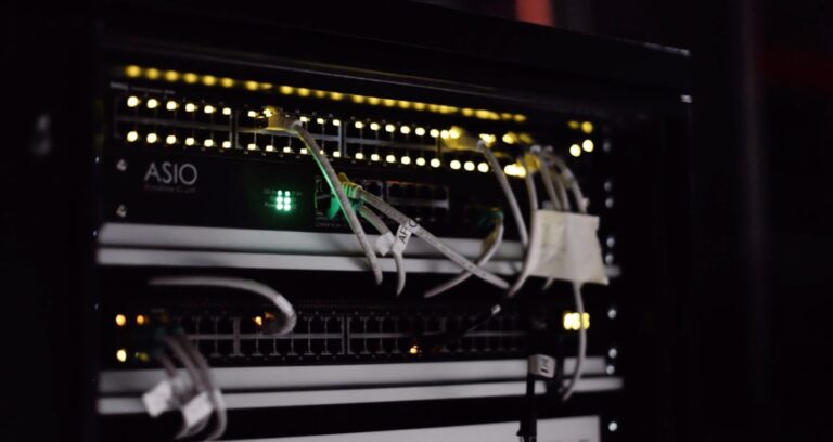 Rack de red con switches, luces de estado y cableado en un armario de comunicaciones.