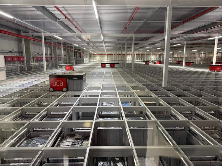 Interior de un sistema AutoStore™ con robots sobre el grid y cubetas de producto en un almacén automatizado.