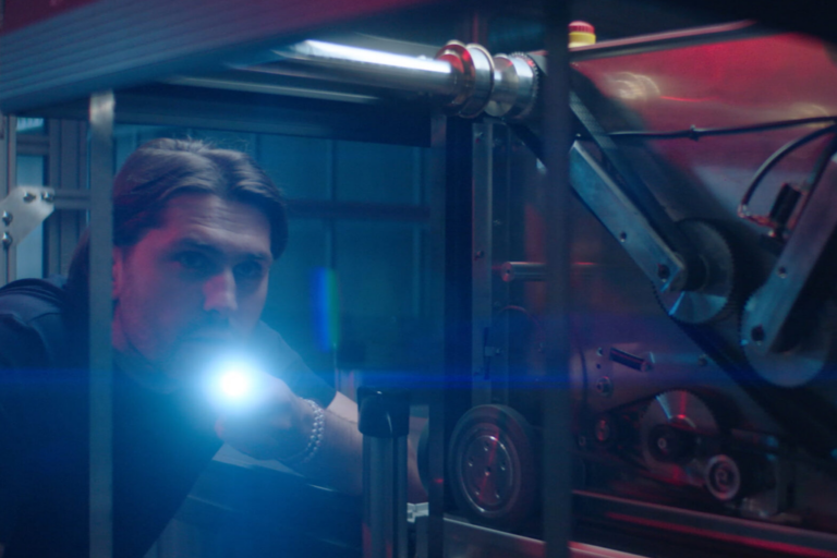 Persona con linterna inspeccionando una máquina o equipo técnico en un entorno industrial.
