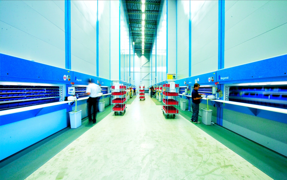Operarios trabajando en un almacén automatizado con sistemas verticales de almacenamiento y preparación de pedidos.