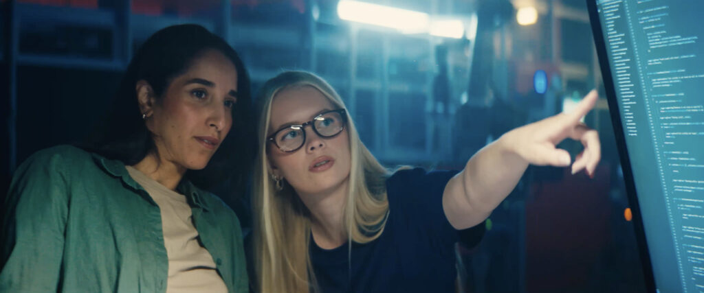 A picture of two women collaborating in front of a computer with warehouse automation in the background.