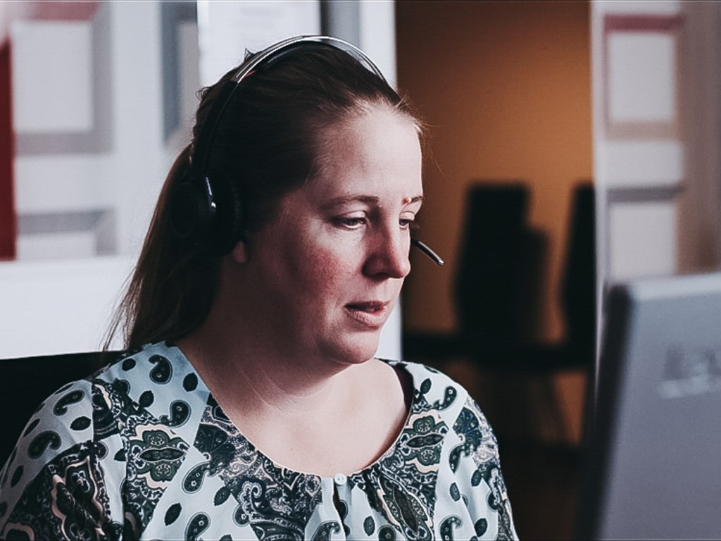 A close-up of a woman talking in headphones in front of a computer.