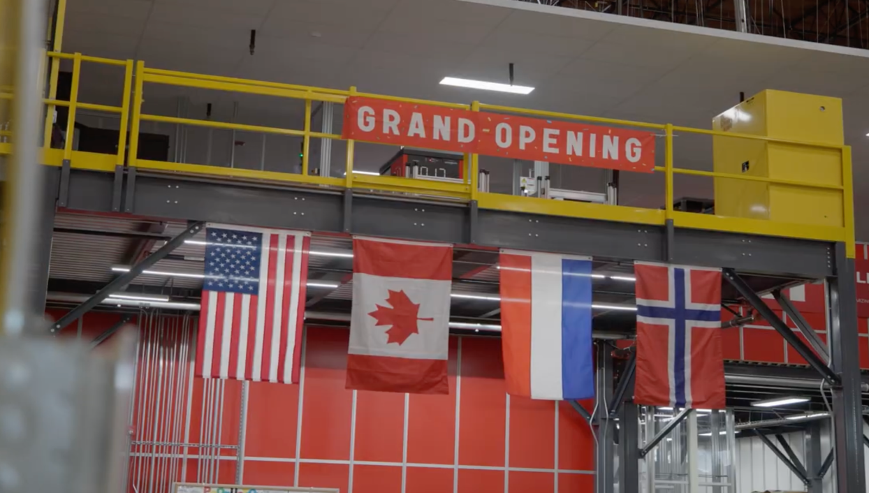 Picture of a banner stating the grand opening of the warehouse with flags